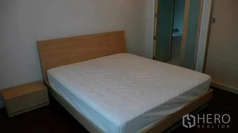 Condominium for rent in Ratchathewi, Bangkok - Minimalist bedroom with wooden bed frame, mattress and bedside table.
