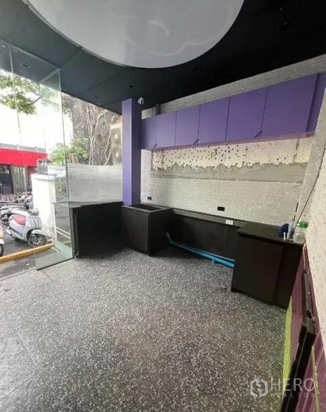 Retail Space for rent in Watthana, Bangkok - Interior view toward the glass entrance with built-in counter, purple cabinets, and street visibility.
