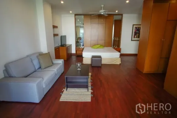 Apartment for rent in Watthana, Bangkok - Large master bedroom with wood flooring, ceiling fan, sofa corner, built-in wardrobes, and TV console.