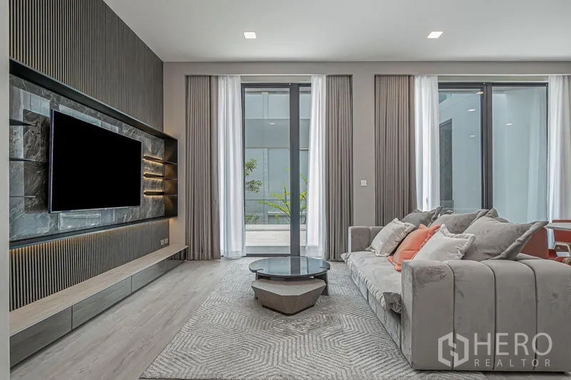 Detached House for rent - Living room with TV feature wall, large windows and a plush sofa.