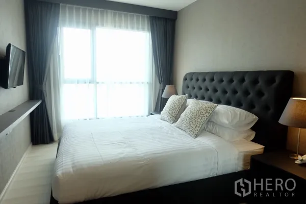 Condominium for rent in Khlong Toei, Bangkok - Master bedroom with tufted headboard, wall‑mounted TV, large windows and twin lamps at Life Condominium.