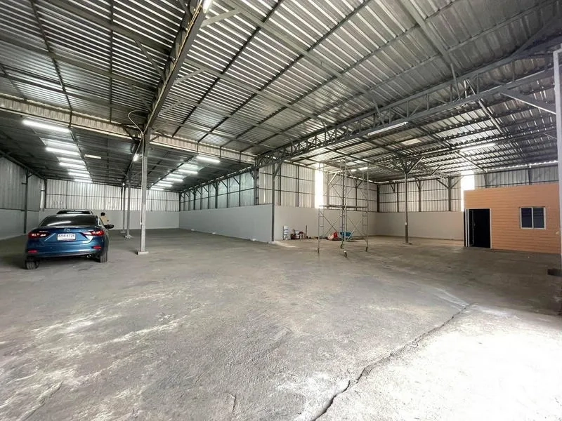 Warehouse for rent in Nakhon Pathom - Spacious warehouse interior with high steel trusses, bright lighting, and open parking space.