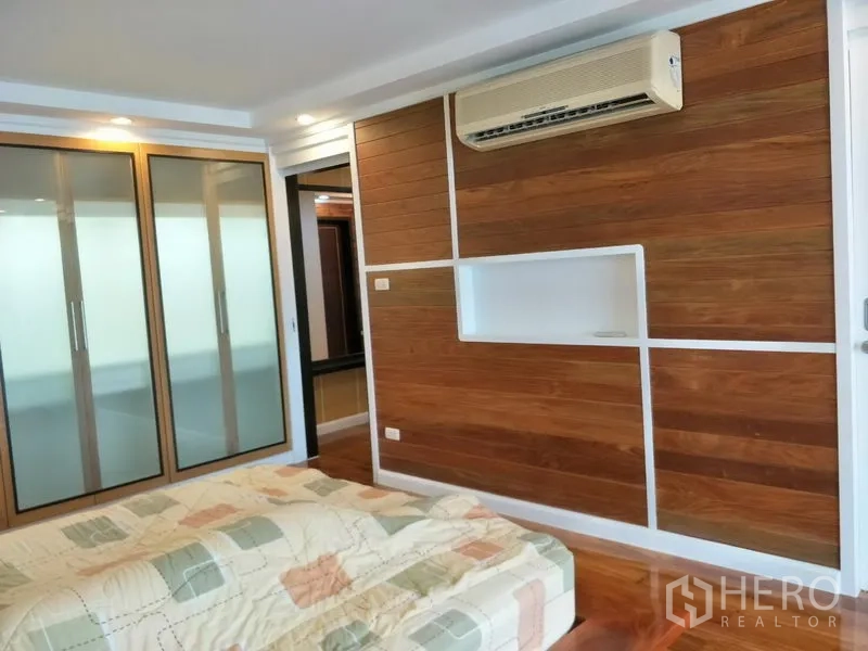 Condominium for rent or sale in Watthana, Bangkok - Bedroom interior showing a wood accent wall, air conditioner and built‑in storage.