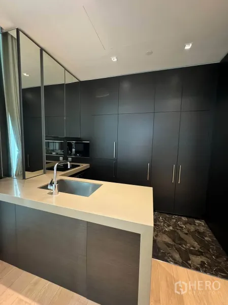 Condominium for rent in Pathum Wan, Bangkok - Modern open kitchen with island sink, light countertop, and tall dark cabinetry.