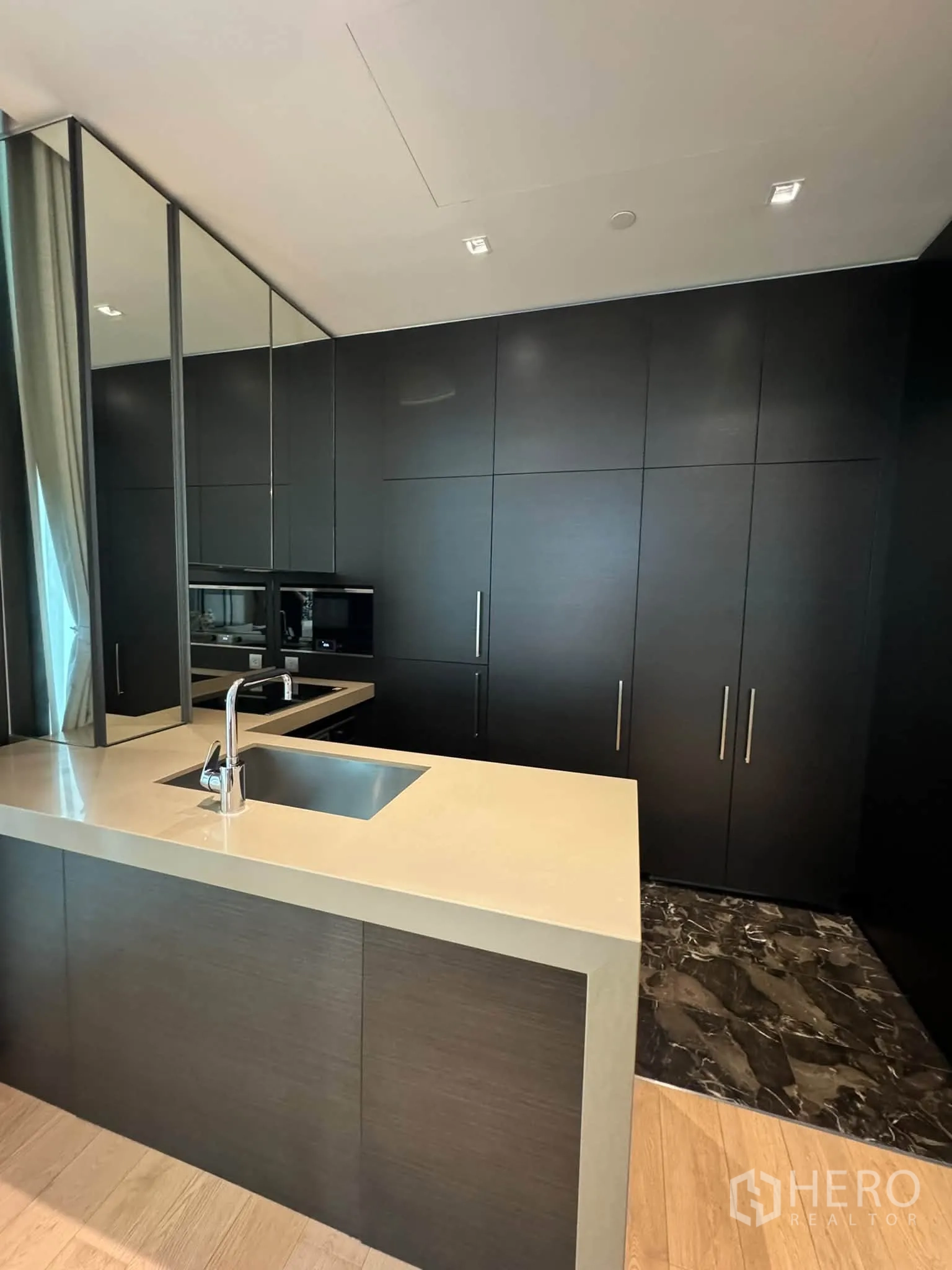 Condominium for rent in Pathum Wan, Bangkok - Modern open kitchen with island sink, light countertop, and tall dark cabinetry.