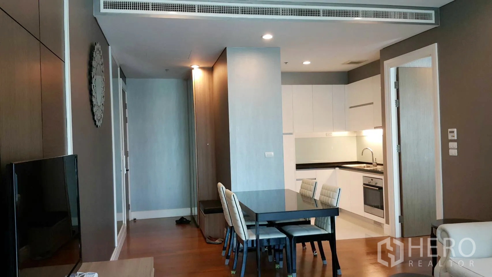 Condominium for rent in Khlong Toei, Bangkok - Open-plan living and dining area with fitted white kitchen and wooden floor.