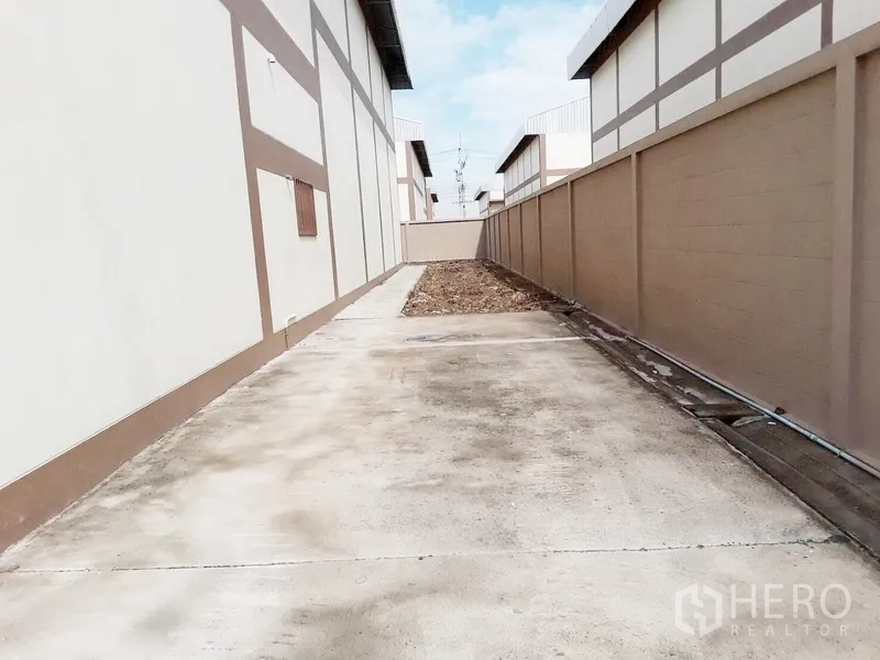 Factory for rent or sale in Pathum Thani - Concrete side driveway between factory buildings bordered by high walls.