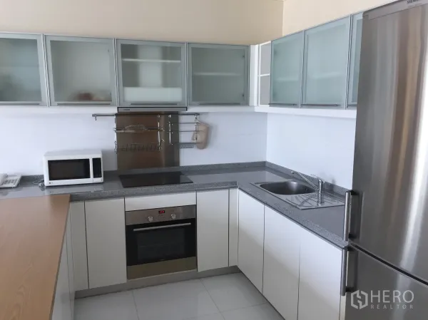 Condominium for rent in Khlong Toei, Bangkok - Modern U-shaped kitchen with granite countertops, glass-front cabinets, built-in oven, induction hob, microwave, and stainless refrigerator.