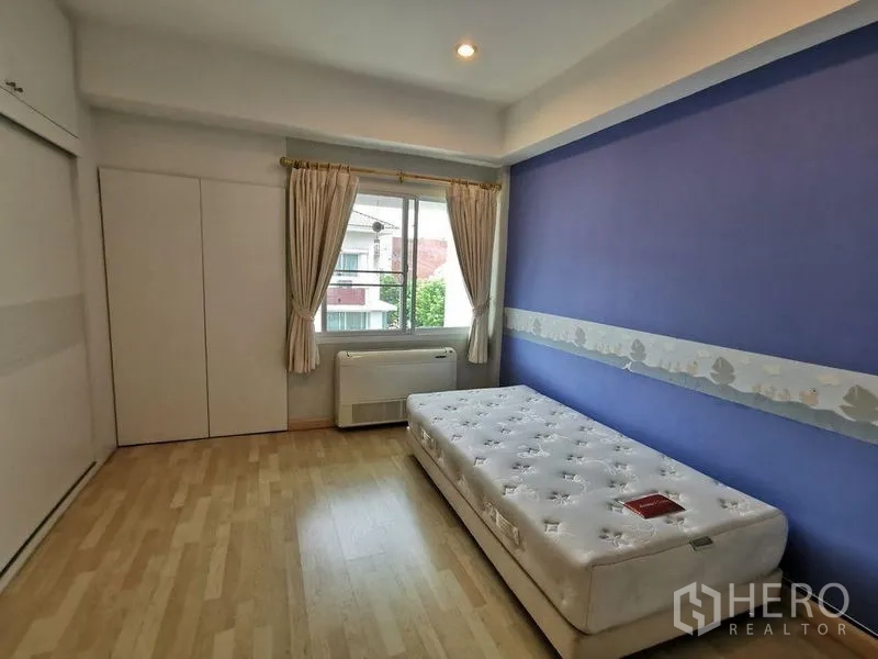 Townhouse for rent or sale in Yan Nawa, Bangkok - Bright bedroom with single bed, blue feature wall, window and built-in wardrobe.