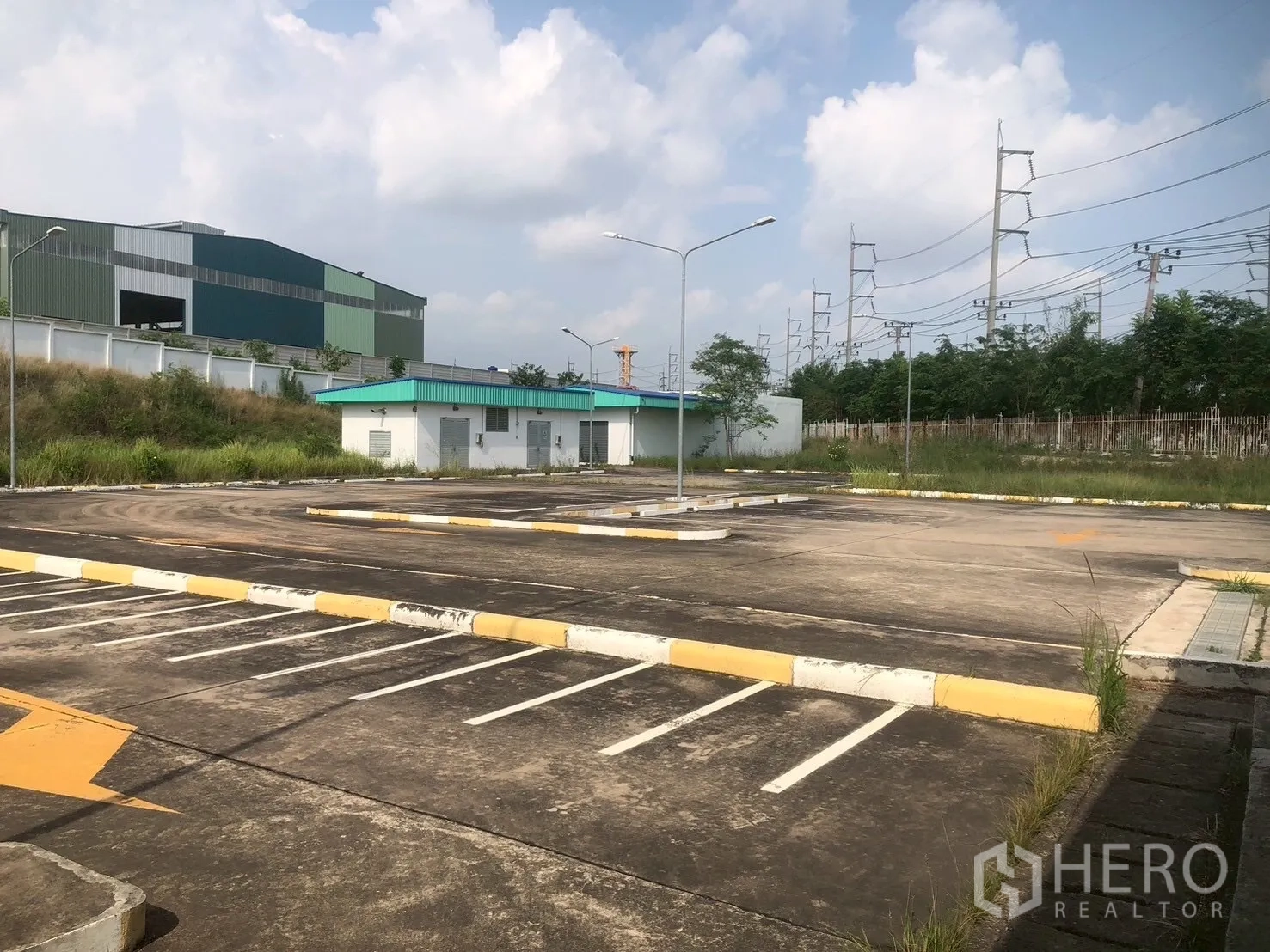 Factory for rent in Pluak Daeng, Rayong - Open parking lot with marked spaces, streetlights, and small utility buildings.