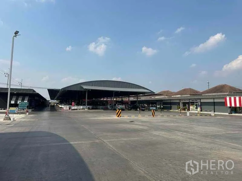 Retail Space for rent in Pathum Thani - Wide concrete forecourt with covered market pavilions and easy vehicle access under a clear sky.
