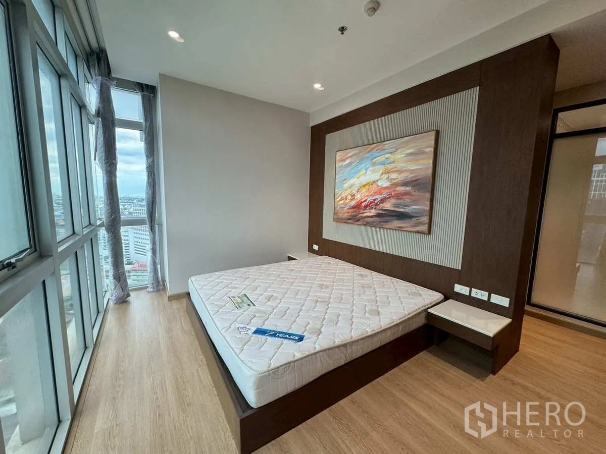 Condominium for rent or sale in Khlong Toei, Bangkok - Bedroom with city-view corner windows and wall-mounted artwork.