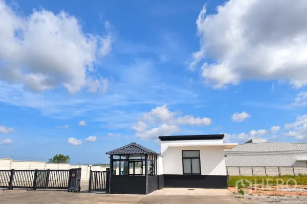 Warehouse for rent in Si Racha, Chon Buri - Entrance area with security booth, sliding gate, and perimeter fence at the warehouse.