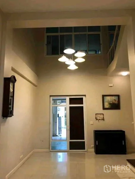 Townhouse for rent in Phra Khanong, Bangkok - Foyer with mezzanine, pendant chandelier and glass door to the rear.