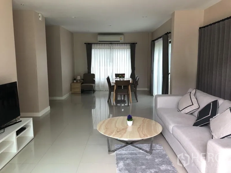 Detached House for rent or sale in Bang Kapi, Bangkok - Spacious living room with sofa, TV console and dining zone, tiled floors and curtain-lined windows.
