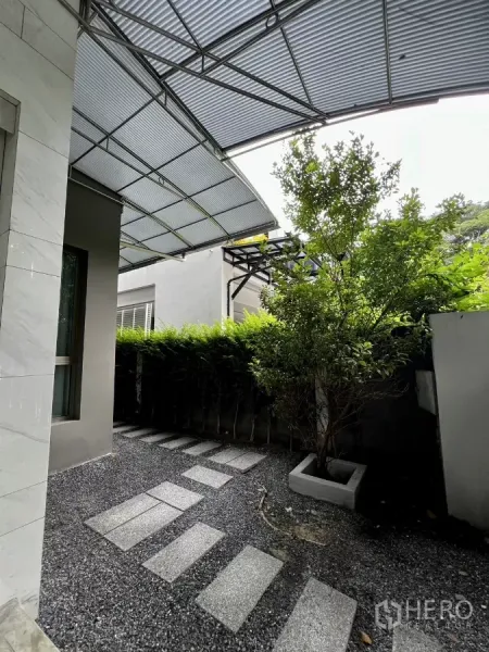 Detached House for rent or sale in Prawet, Bangkok - Low-maintenance side yard with stepping stones, hedges and a polycarbonate canopy.