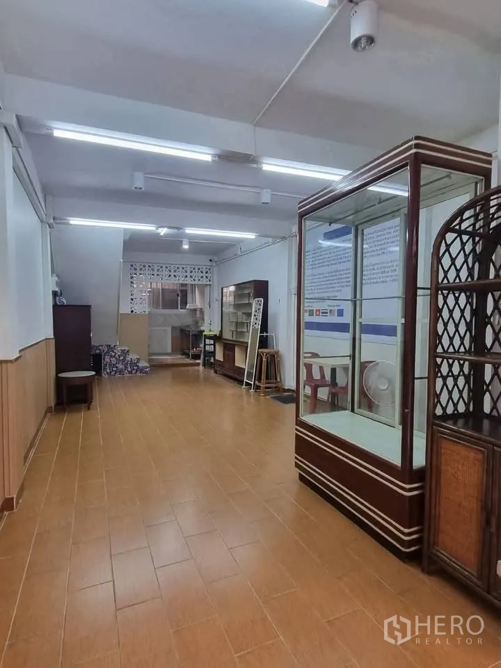 Shophouse for rent in Phra Khanong, Bangkok - Long ground-floor hall with tile floors, glass display units, and stairs at the rear.