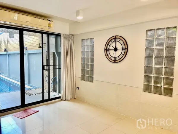 联排别墅 出租在Khlong Toei, Bangkok - 客厅墙面装饰钟，落地推拉门通向私家泳池。
