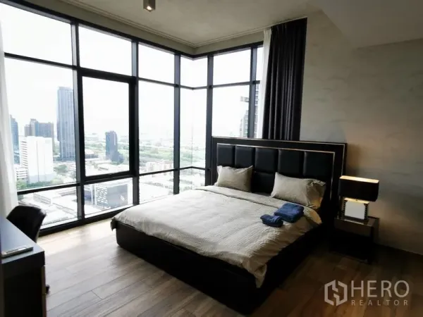 公寓 出租在Watthana, Bangkok - 转角主卧配落地全景窗，城市景观尽收眼底，软包床头与床头灯。