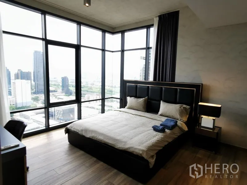 公寓 出租在Watthana, Bangkok - 转角主卧配落地全景窗，城市景观尽收眼底，软包床头与床头灯。