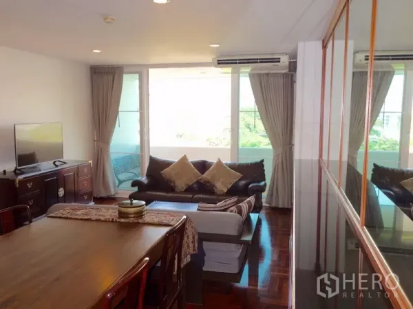 Condominium for rent or sale in Watthana, Bangkok - Bright lounge with floor-to-ceiling windows, balcony access, curtains and TV console.