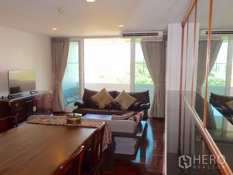 Condominium for rent or sale in Watthana, Bangkok - Bright lounge with floor-to-ceiling windows, balcony access, curtains and TV console.