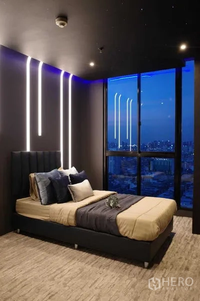 Condominium for sale - Modern bedroom with accent lighting and floor-to-ceiling window overlooking the Bangkok skyline at dusk.