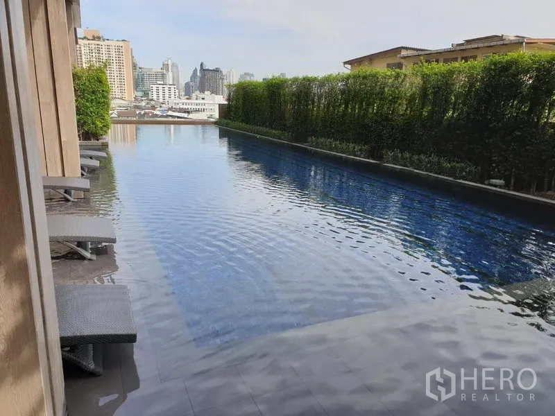 公寓 出租在Watthana, Bangkok - 长条泳池配躺椅与绿篱，背景为城市天际线。