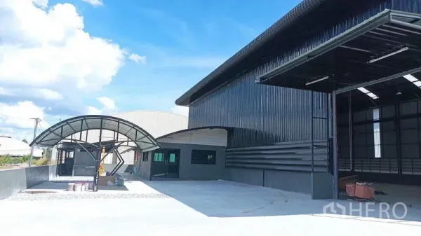 货栈 出租在Ban Bueng, Chon Buri - 仓库立面近景，卷帘装卸口开启，弧形雨棚与宽车道。
