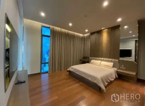Condominium for rent in Khlong Toei, Bangkok - Spacious master bedroom with wood flooring, recessed lighting, floor-to-ceiling window and full-length curtains with city view.