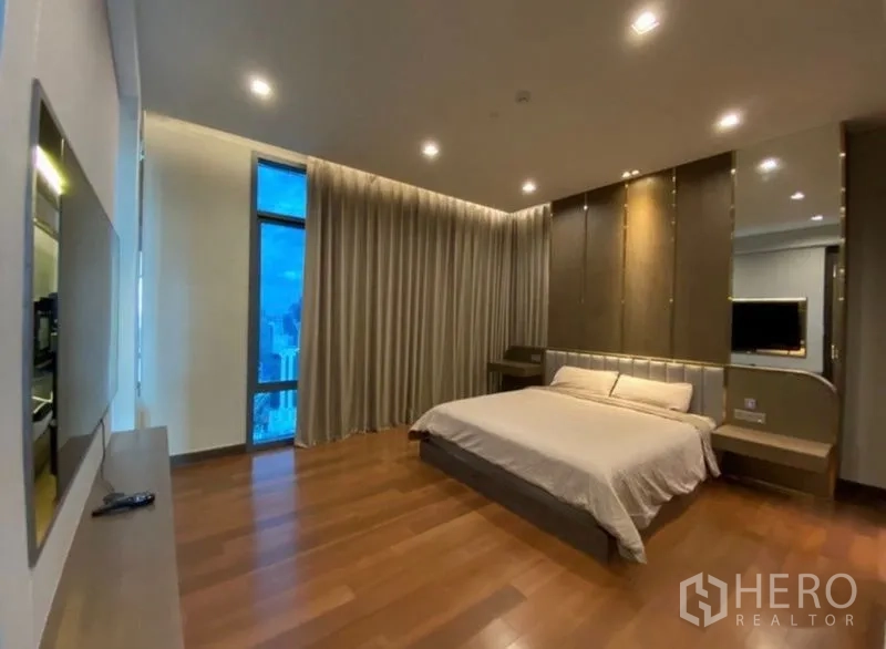 Condominium for rent in Khlong Toei, Bangkok - Spacious master bedroom with wood flooring, recessed lighting, floor-to-ceiling window and full-length curtains with city view.
