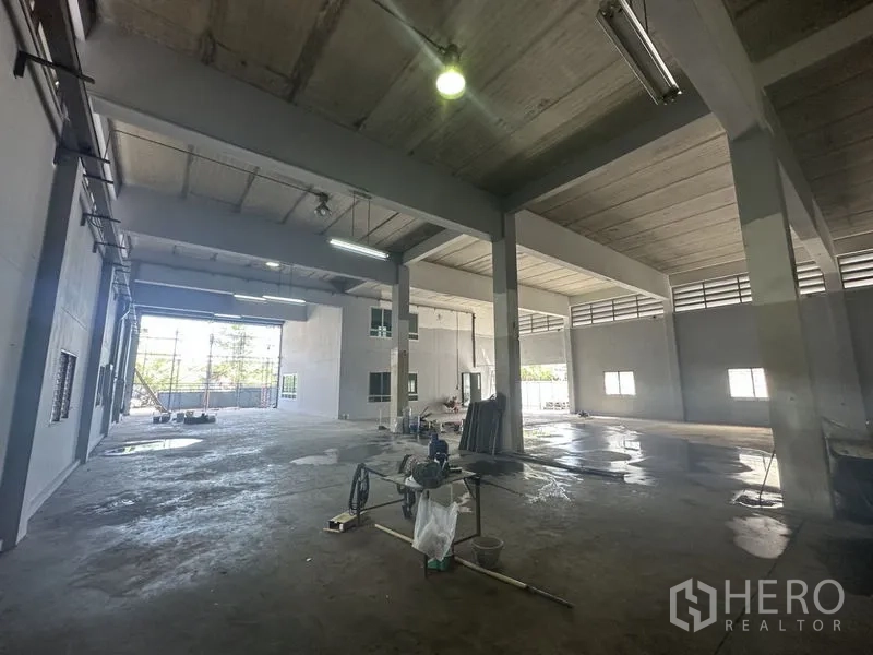 Factory for rent or sale in Bang Bua Thong, Nonthaburi - Deep warehouse hall showing roll-up entry, skylights and ample maneuvering space.