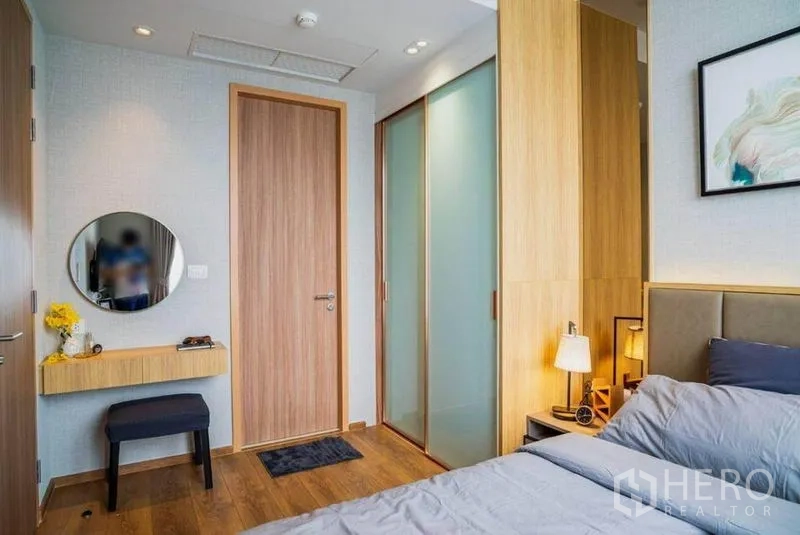公寓 出租在Watthana, Bangkok - 卧室铺木地板，悬空梳妆台、磨砂玻璃衣柜与温暖床头灯。