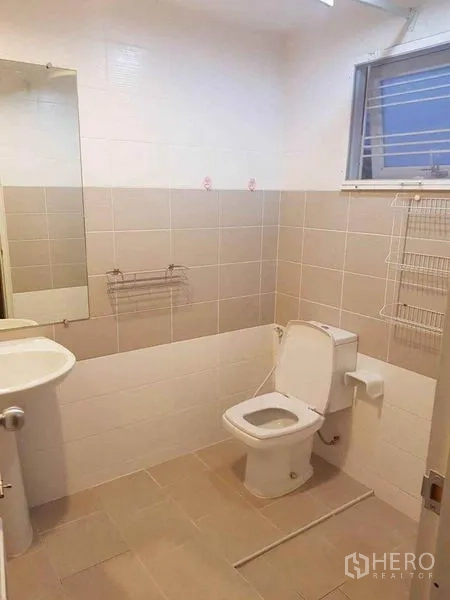 Detached House for sale in Nonthaburi - Clean tiled bathroom with toilet, sink, wall mirror and a louvered window.
