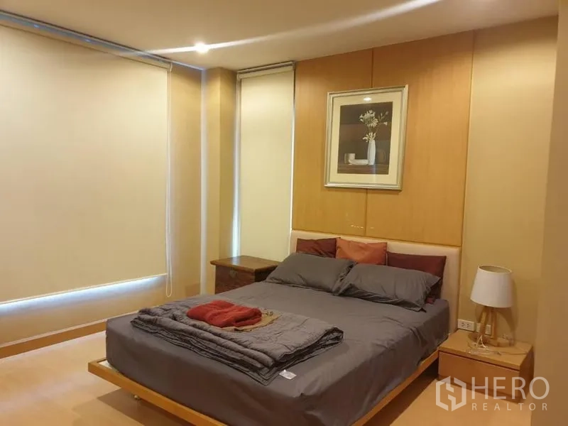 คอนโด ให้เช่าในWatthana, Bangkok - ห้องนอนหลักเตียงควีน โต๊ะข้างเตียง มู่ลี่ทึบแสง และผนังไม้โทนอุ่น