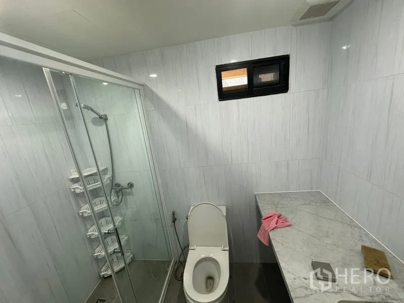 公寓 出租在Watthana, Bangkok - 明亮卫生间，设玻璃淋浴间、大理石台面和小通风窗。