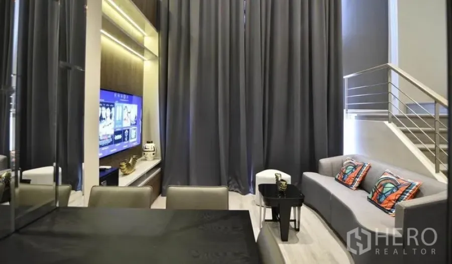 คอนโด ให้เช่าในHuai Khwang, Bangkok - ห้องนั่งเล่นเพดานสูง ผ้าม่านสีเทา โซฟา ผนังทีวี และโต๊ะทานข้าว