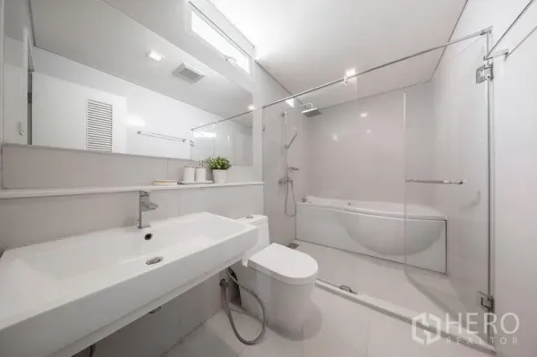 Condominium for rent or sale in Watthana, Bangkok - Bright modern bathroom with long vanity, glass-enclosed shower and bathtub.