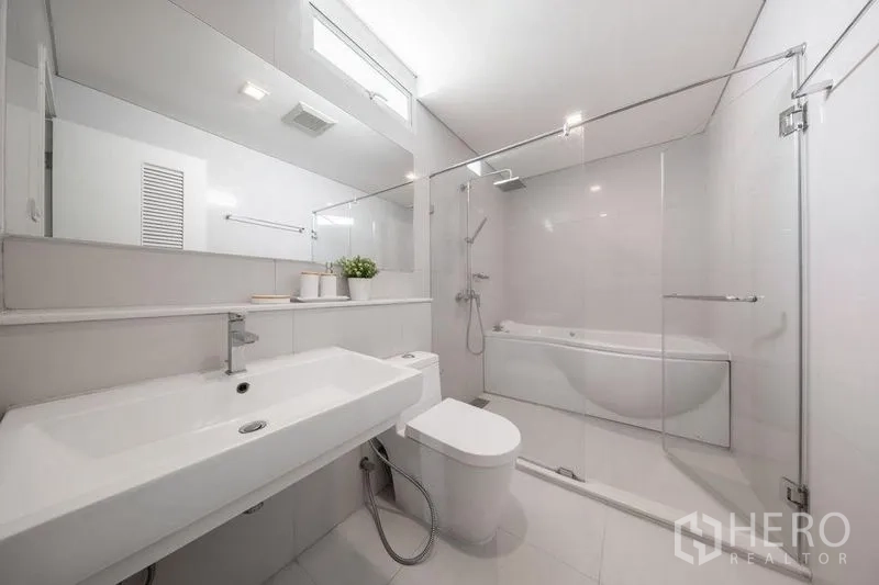 Condominium for rent or sale in Watthana, Bangkok - Bright modern bathroom with long vanity, glass-enclosed shower and bathtub.