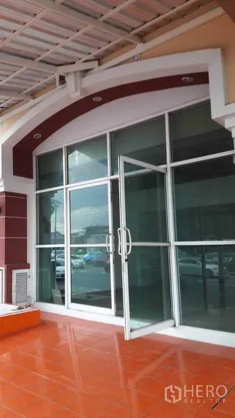 办公空间 出租在Bueng Kum, Bangkok - 整面玻璃门窗的建筑外立面，带遮棚和橙色地砖平台。