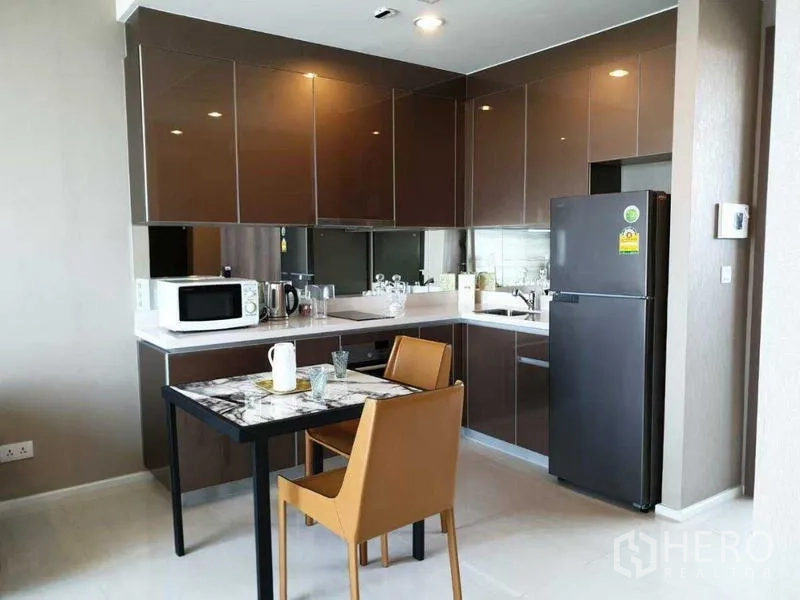 Condominium for rent in Bang Kho Laem, Bangkok - Modern kitchen with glossy cabinets, dining table, and appliances.