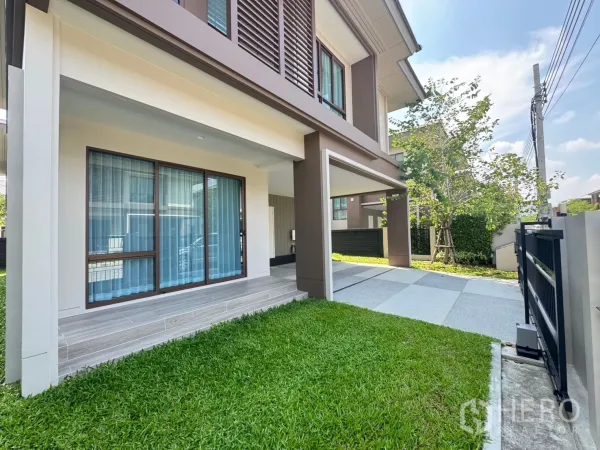 Detached House for rent or sale in Bang Kapi, Bangkok - Front lawn and terrace with sliding glass doors leading to a shaded parking area.