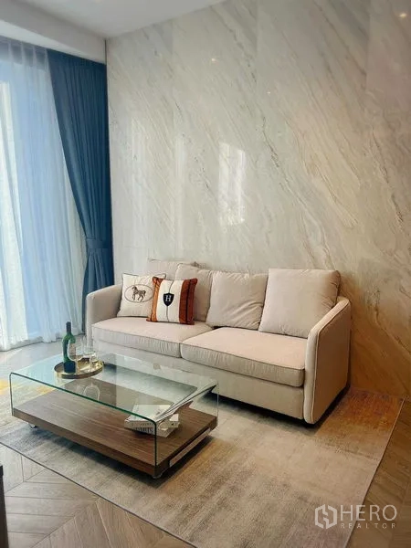Condominium for rent in Khlong Toei, Bangkok - Bright living room with beige sofa, marble feature wall, and glass coffee table.
