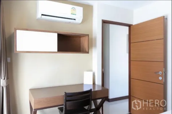 房间 出租在Bang Rak, Bangkok - 紧凑工作角，书桌、墙柜与空调，旁有木门。