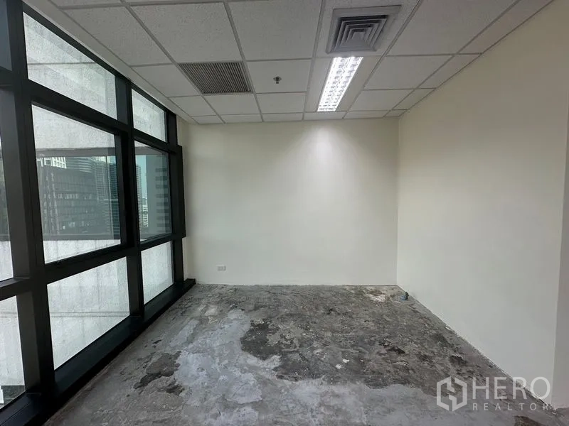 Office Space for rent in Bang Rak, Bangkok - Small private room with large windows, white wall, and raw concrete subfloor ready for customization.