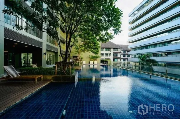 Condominium for rent in Watthana, Bangkok - Outdoor swimming pool with sun loungers, trees, and surrounding modern low-rise buildings.