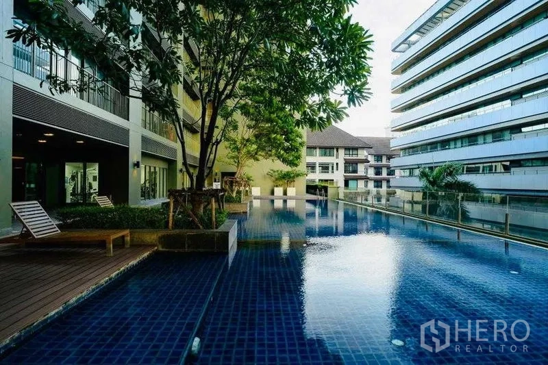 Condominium for rent in Watthana, Bangkok - Outdoor swimming pool with sun loungers, trees, and surrounding modern low-rise buildings.