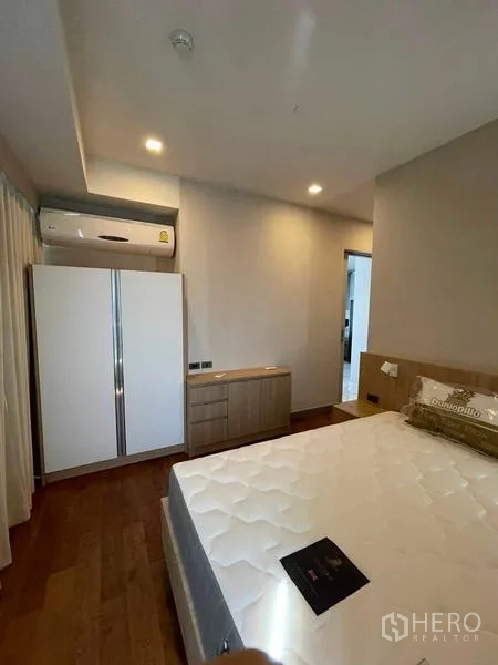 Condominium for rent or sale in Bang Rak, Bangkok - Master bedroom with bed, wardrobe, wooden flooring, and air conditioner.
