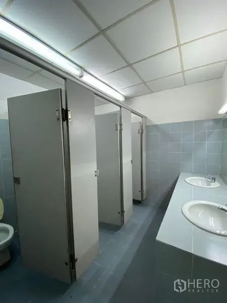Office Space for rent - Clean shared bathroom with multiple cubicles and a double vanity in light gray tiles.