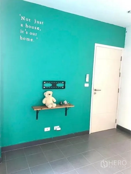 Townhouse for rent in Suan Luang, Bangkok - Living area corner with teal feature wall, small shelf and interior door.